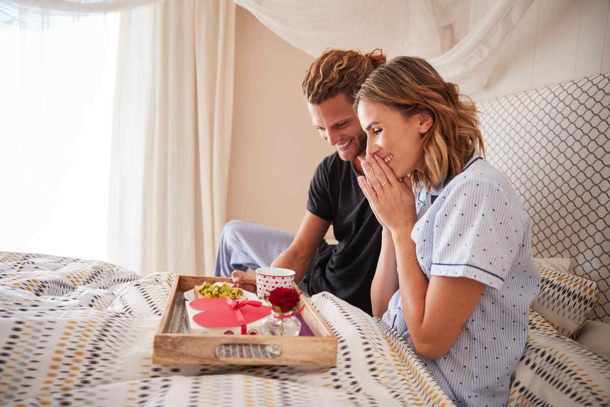 man surprising his female partner with breakfast and gifts in bed